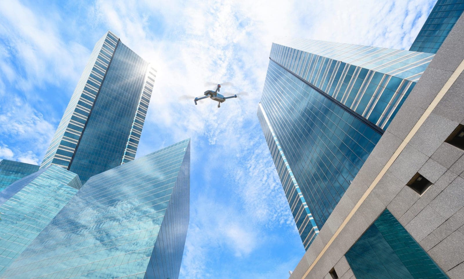 A drone, adhering to strict regulations, flying amidst towering skyscrapers under a partly cloudy sky.