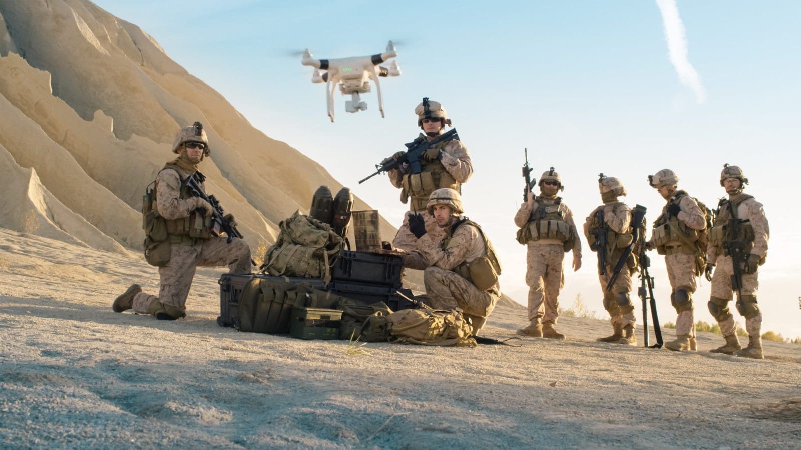 Military personnel engaged in drone warfare, operating a drone in a desert environment.
