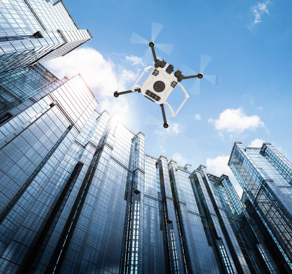 Quadcopter drone flying among modern skyscrapers under a blue sky with clouds, maintaining contact.